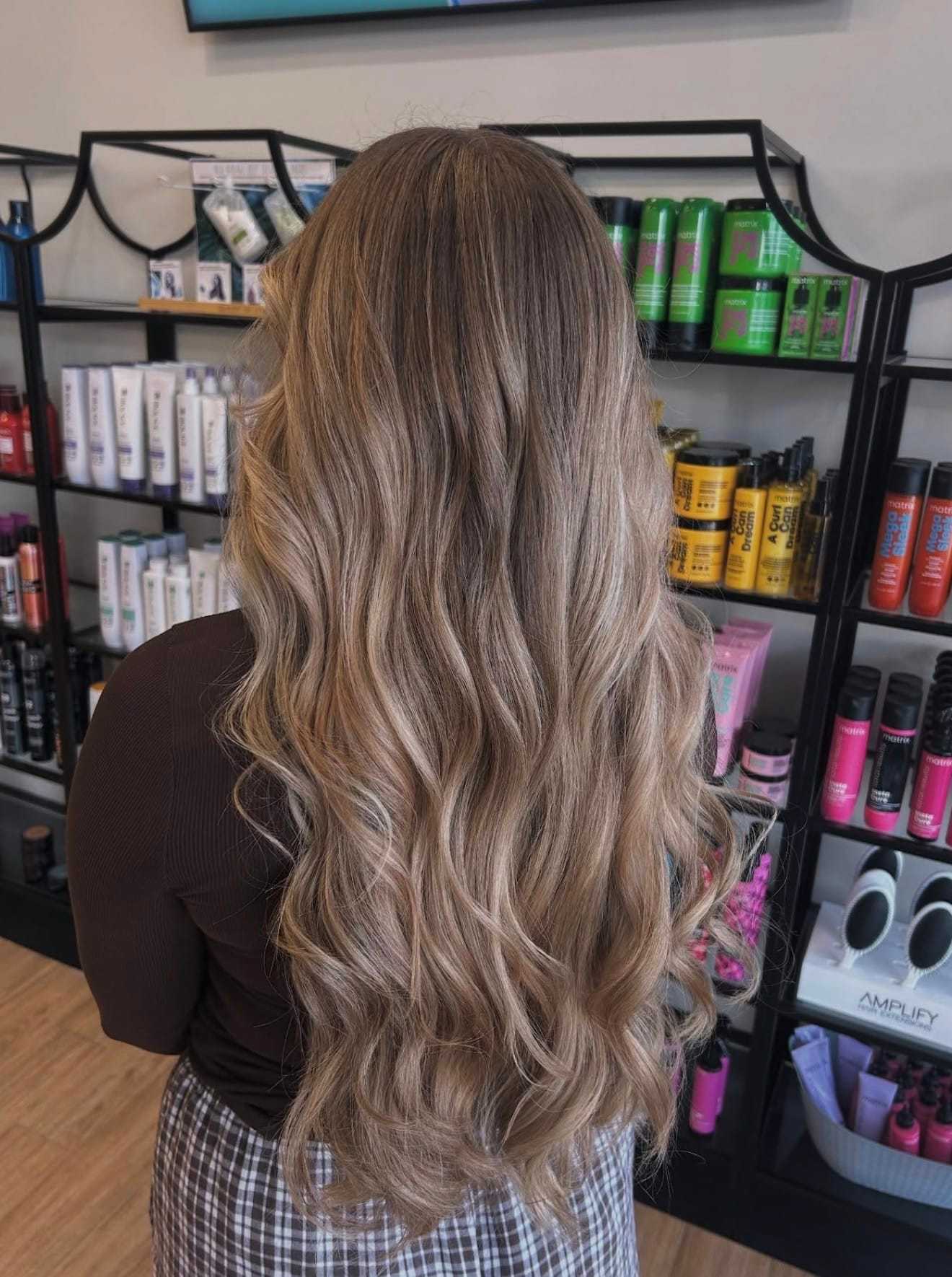 Woman with wavy blonde hair in a salon, standing by shelves of hair products.