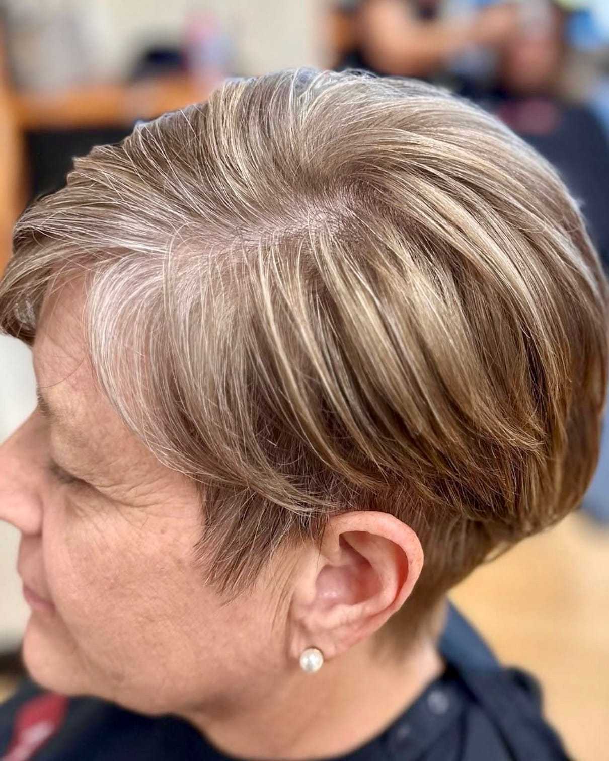 Short-haired woman with layered, highlighted hairstyle in a salon.