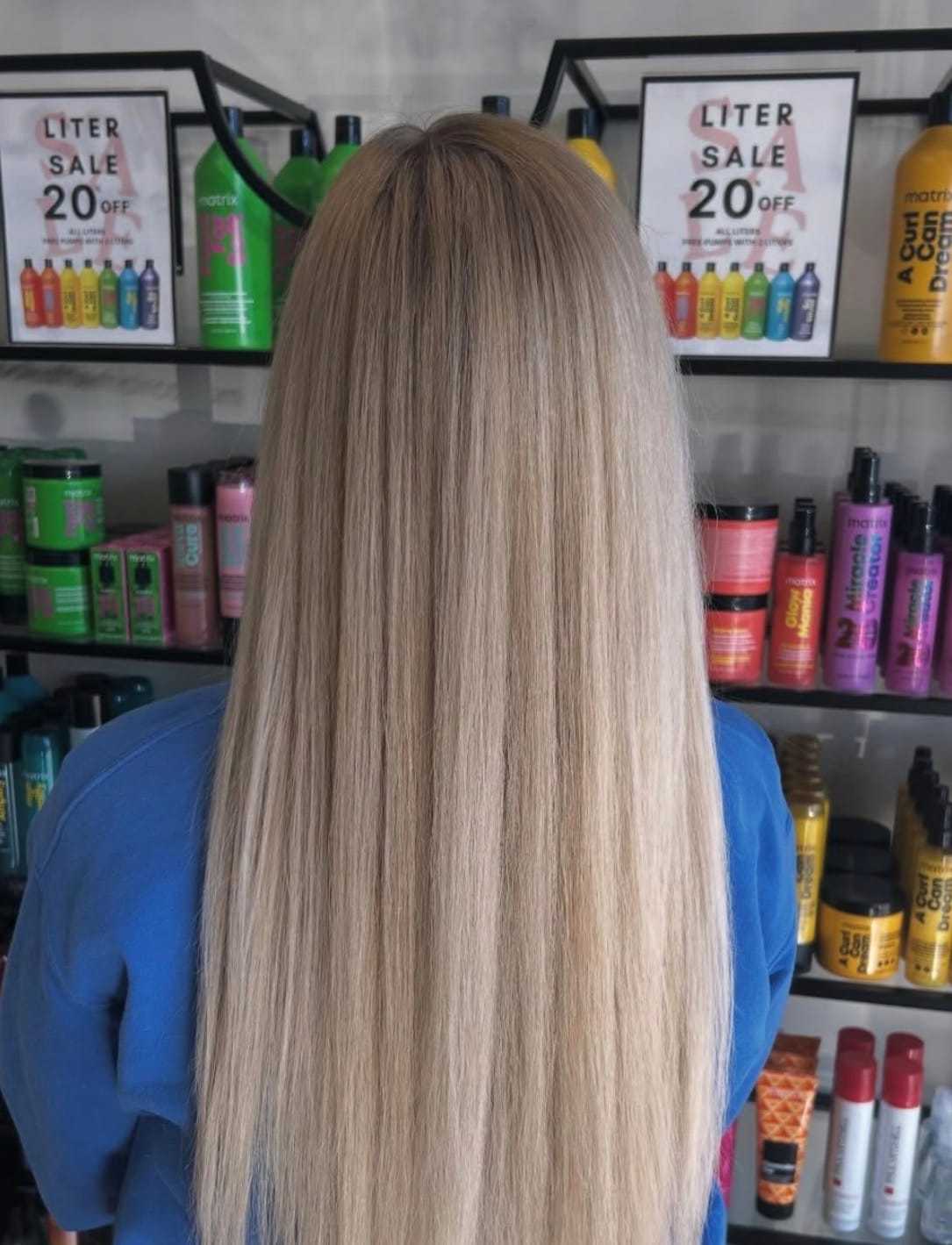 Back view of a person with long, straight blonde hair in a salon with discounted products.