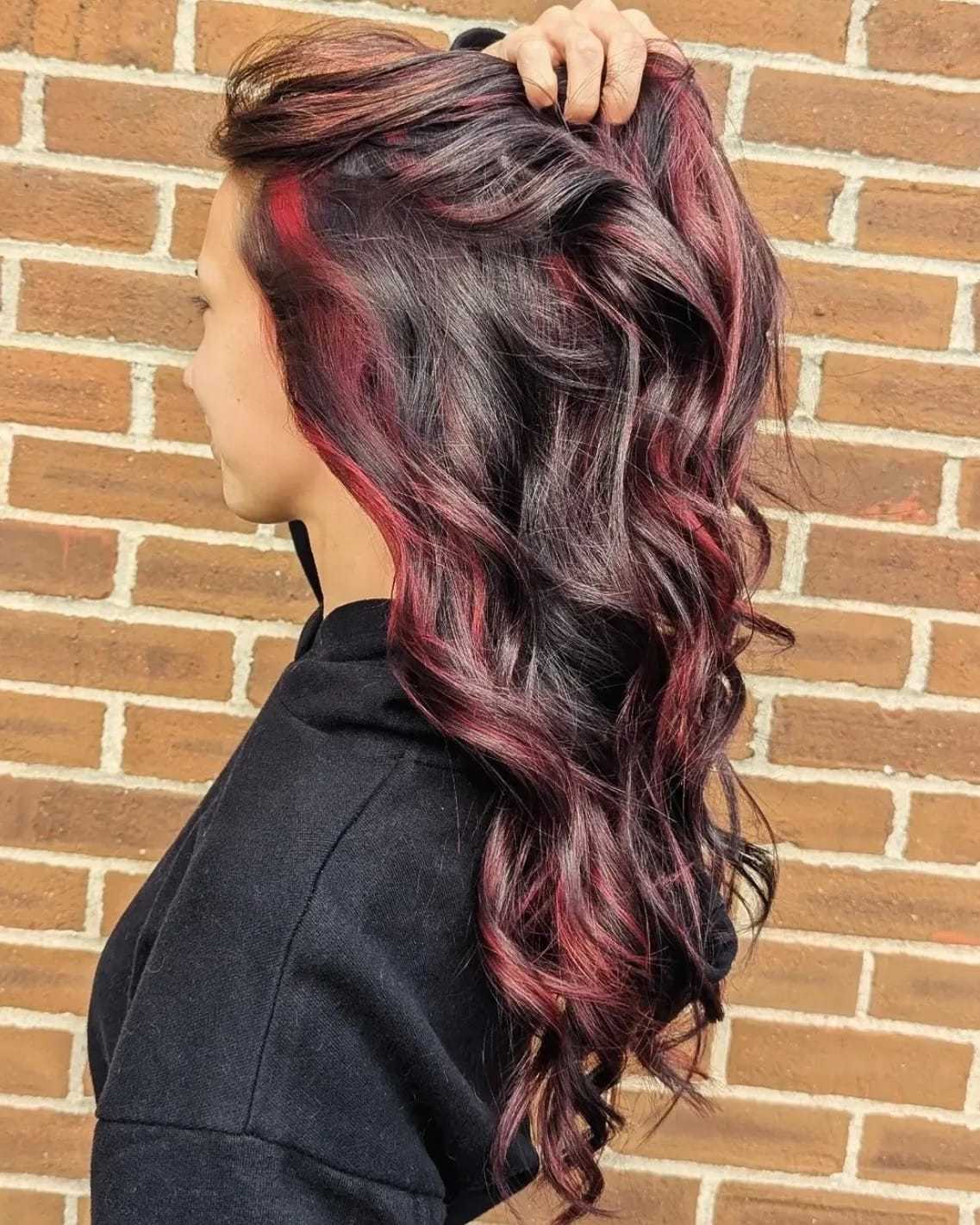 Long wavy hair with vibrant red highlights against a brick wall backdrop.