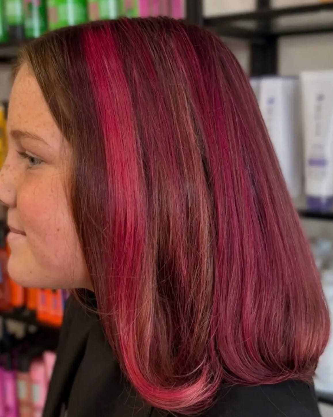 A person with shoulder-length hair dyed in vibrant shades of pink, standing in a salon.