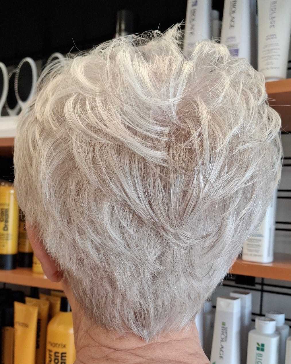 Short silver hairstyle, back view, with layered texture in a salon setting.