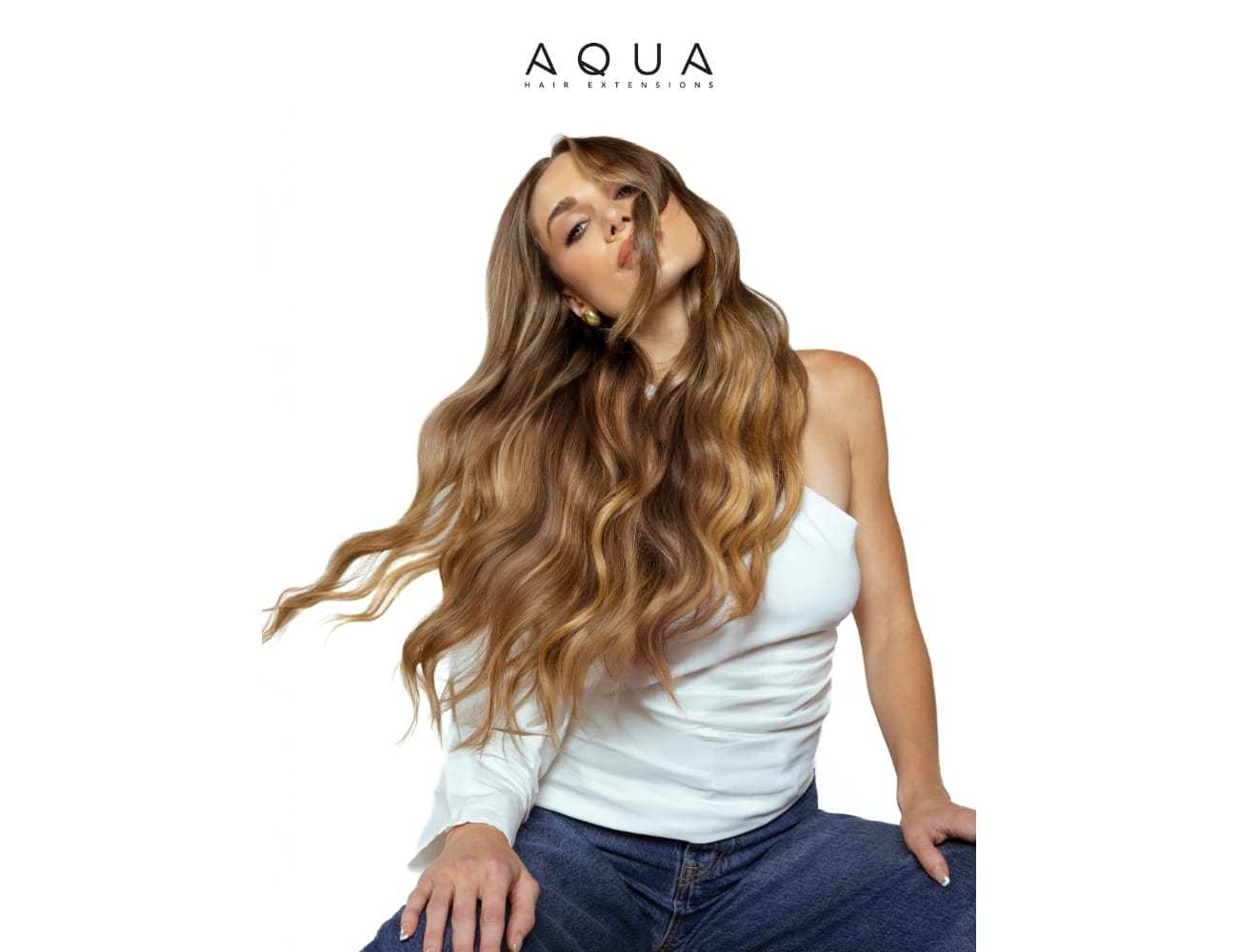 Woman with long, wavy hair wearing a white off-shoulder top and jeans. Brand: Aqua Hair Extensions.
