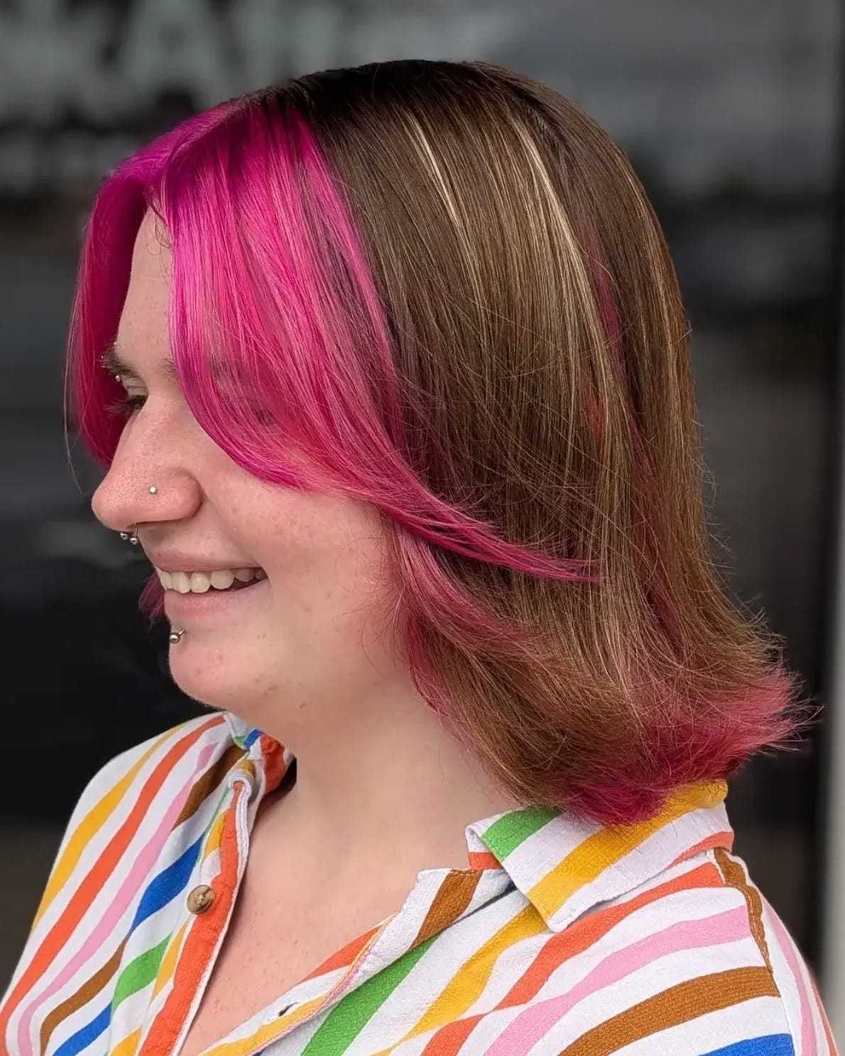 Bright pink highlights in shoulder-length brown hair, person smiling in a striped shirt.