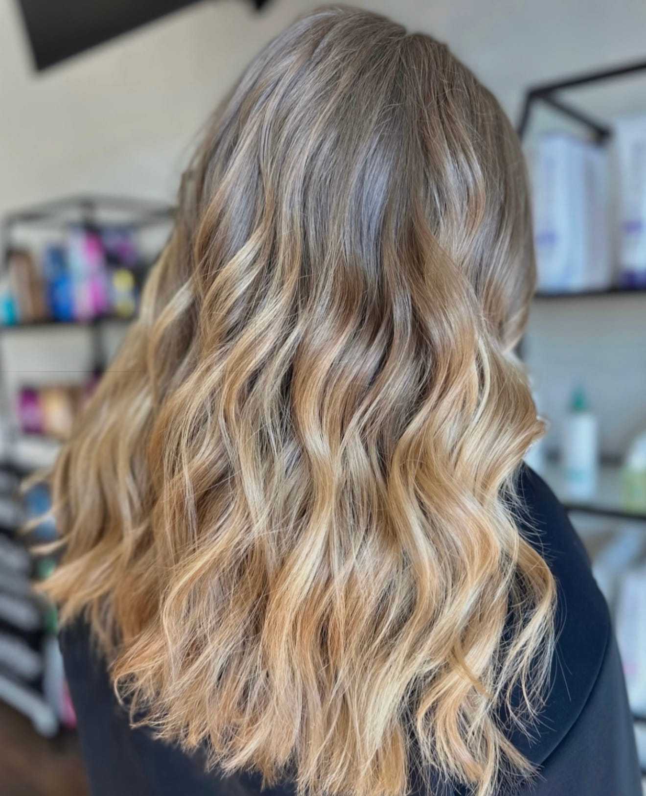 Wavy blonde hair with dark roots viewed from the back in a salon setting.
