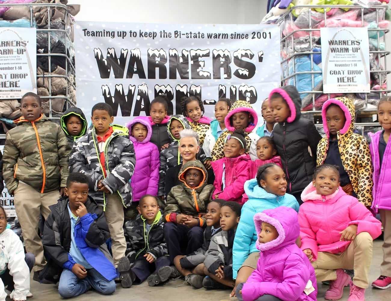 Group of children and an adult at a coat drive event, showcasing donated winter clothing.