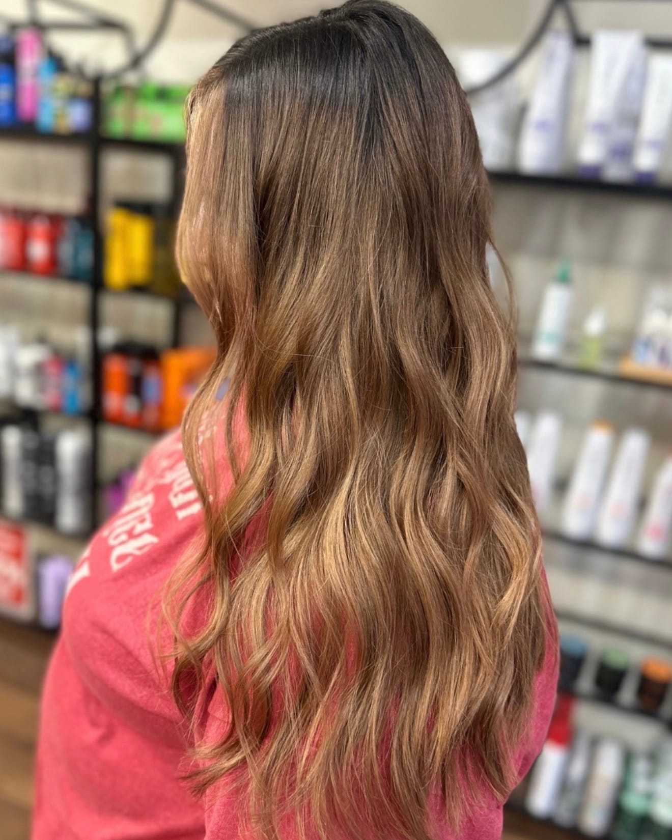 Long wavy hair with light brown highlights, salon shelf background.