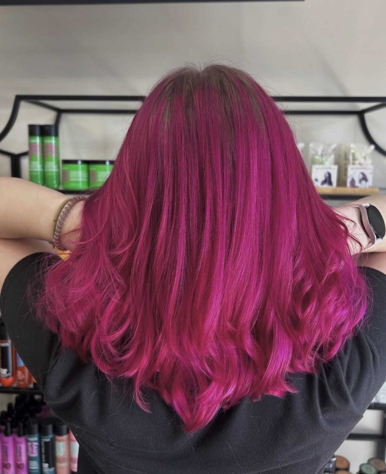 Bright magenta hair styled in loose waves, shown from the back in a salon setting.