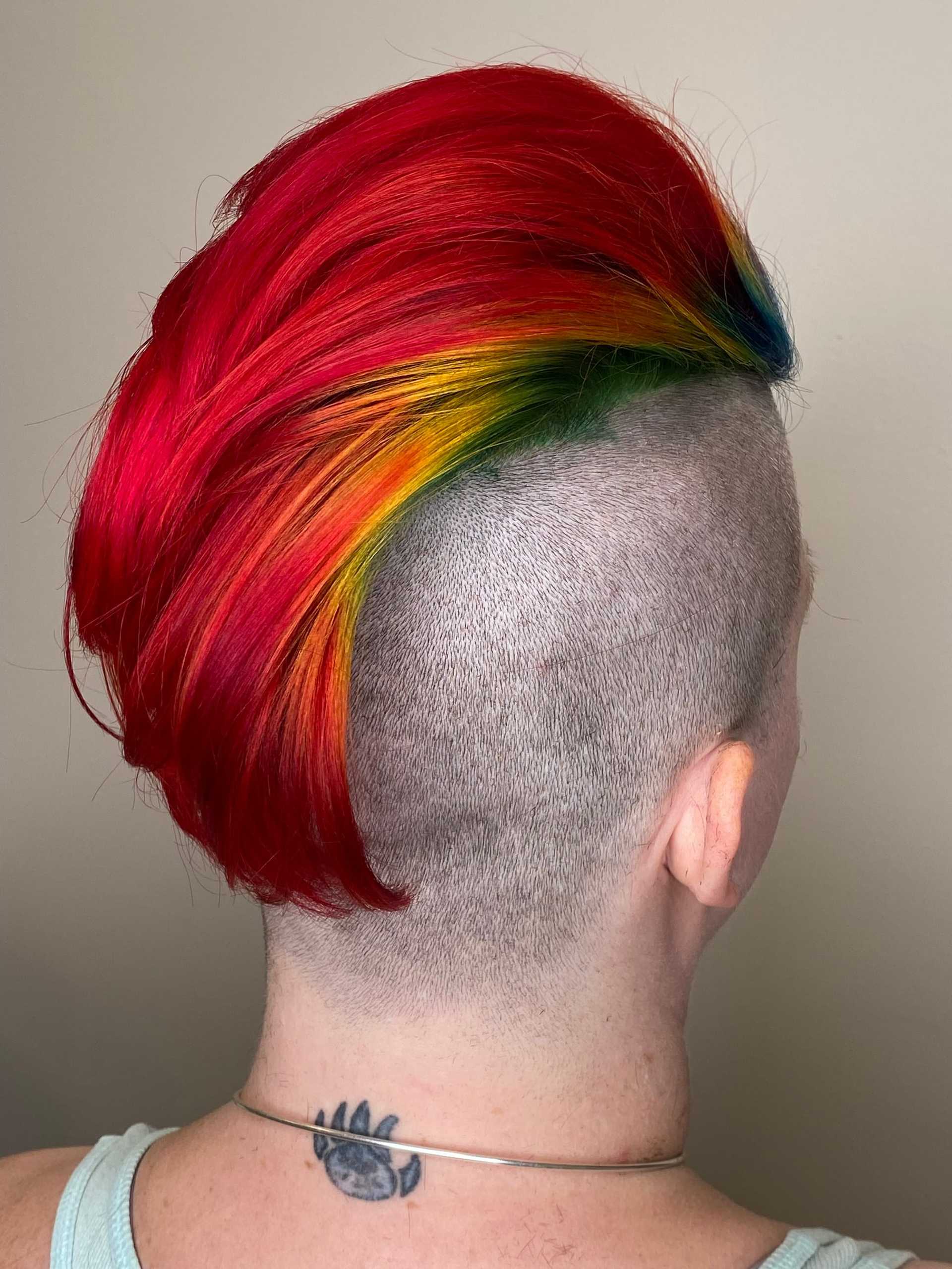 Shaved head with vibrant red and rainbow mohawk hairstyle, bear paw tattoo visible.