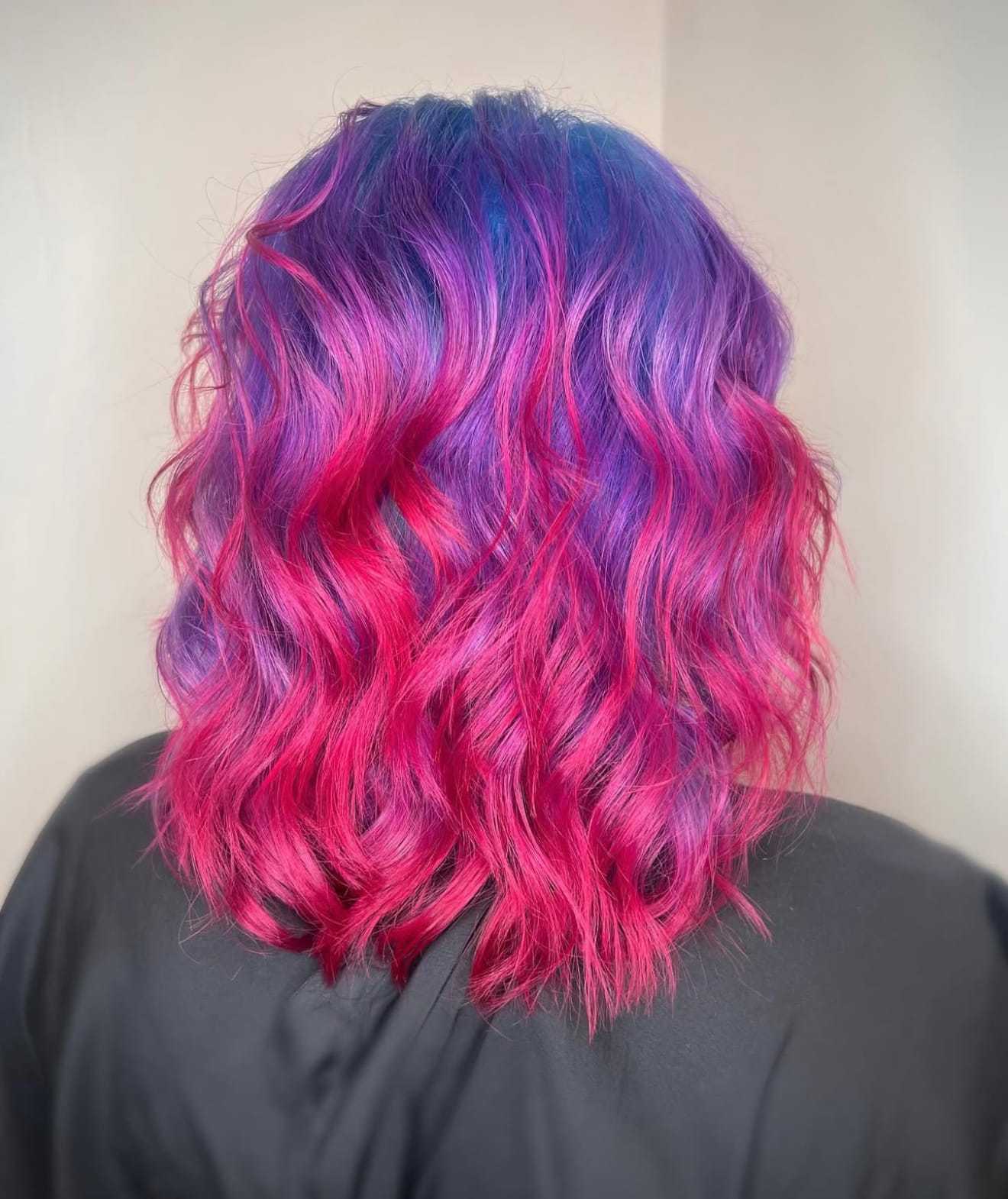 Wavy hair dyed vibrant pink and purple, viewed from the back against a plain background.