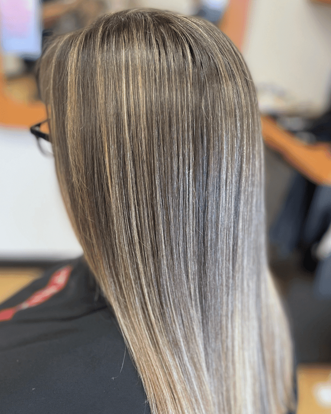 Long straight hair with highlighted streaks, shown from the back in a salon setting.