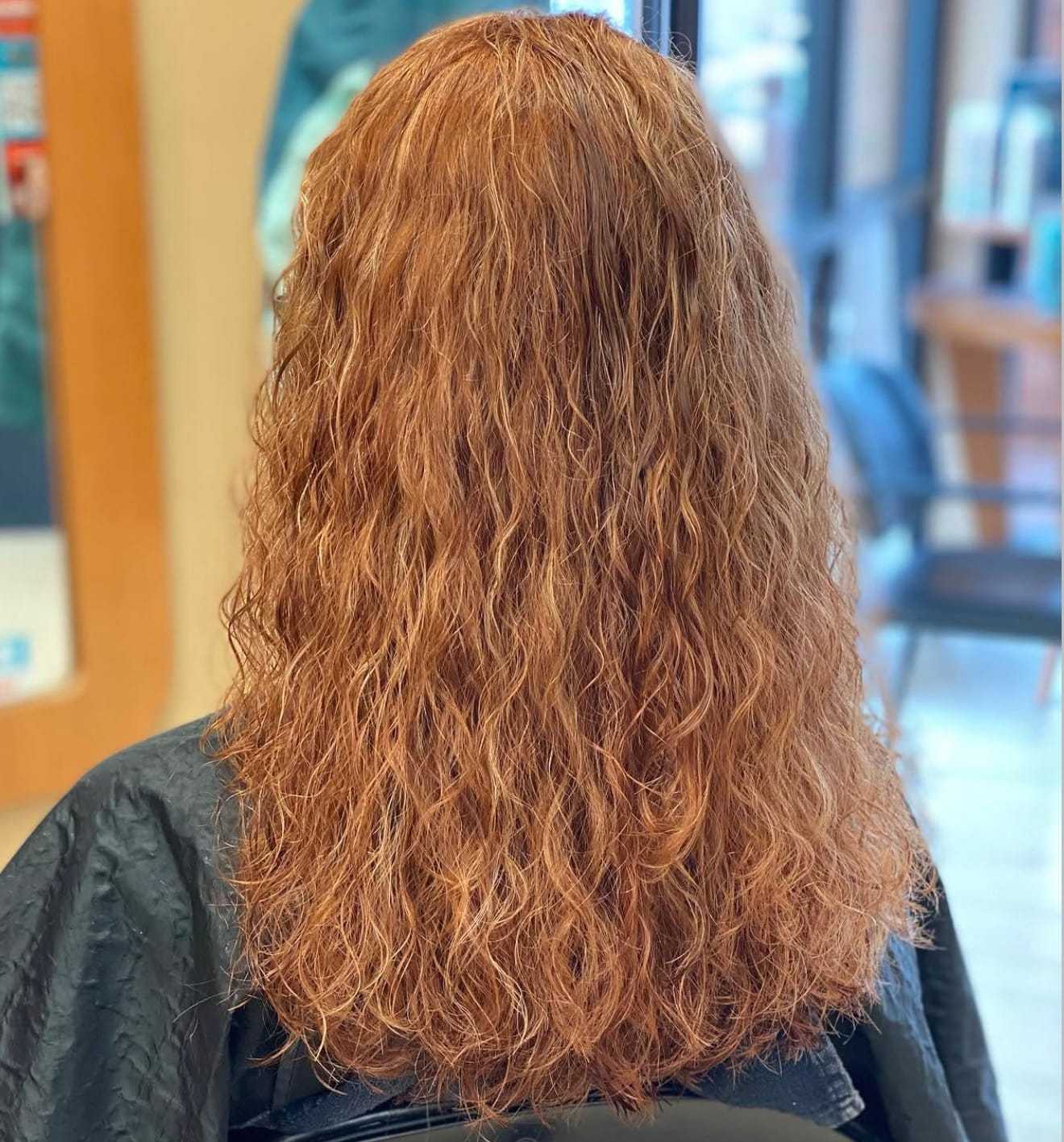 Curly red hair styled in a salon, viewed from the back.