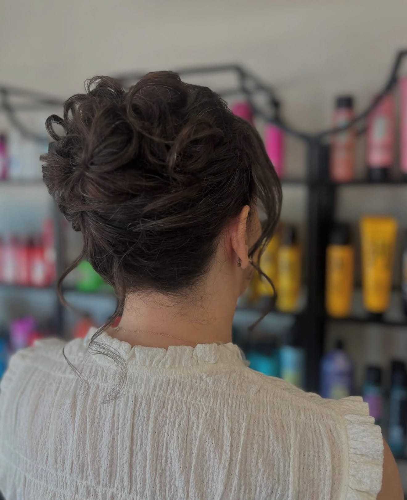 Woman with elegant updo hairstyle in salon, colorful products in background.