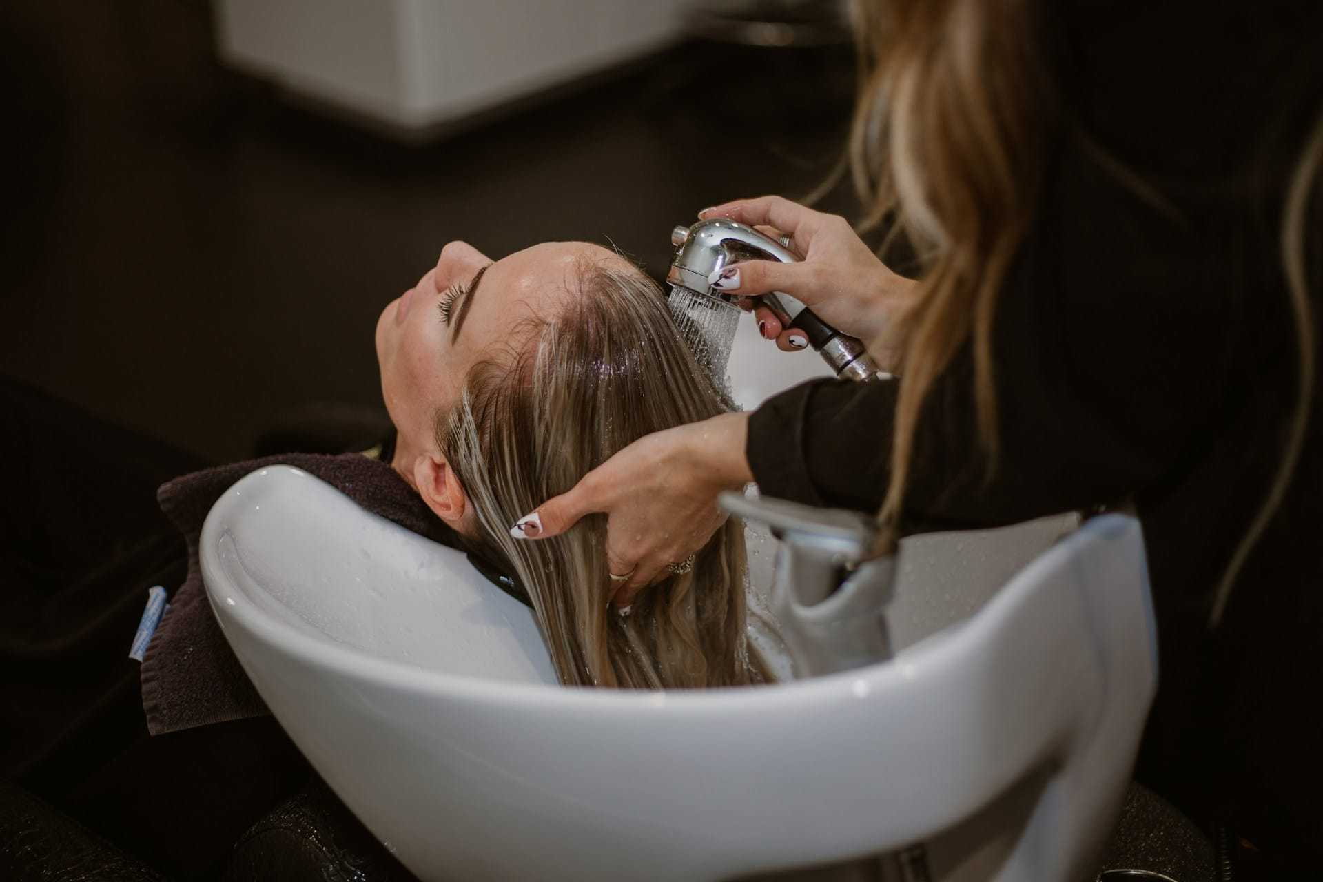 Hairdresser washing a woman's hair at a salon sink.