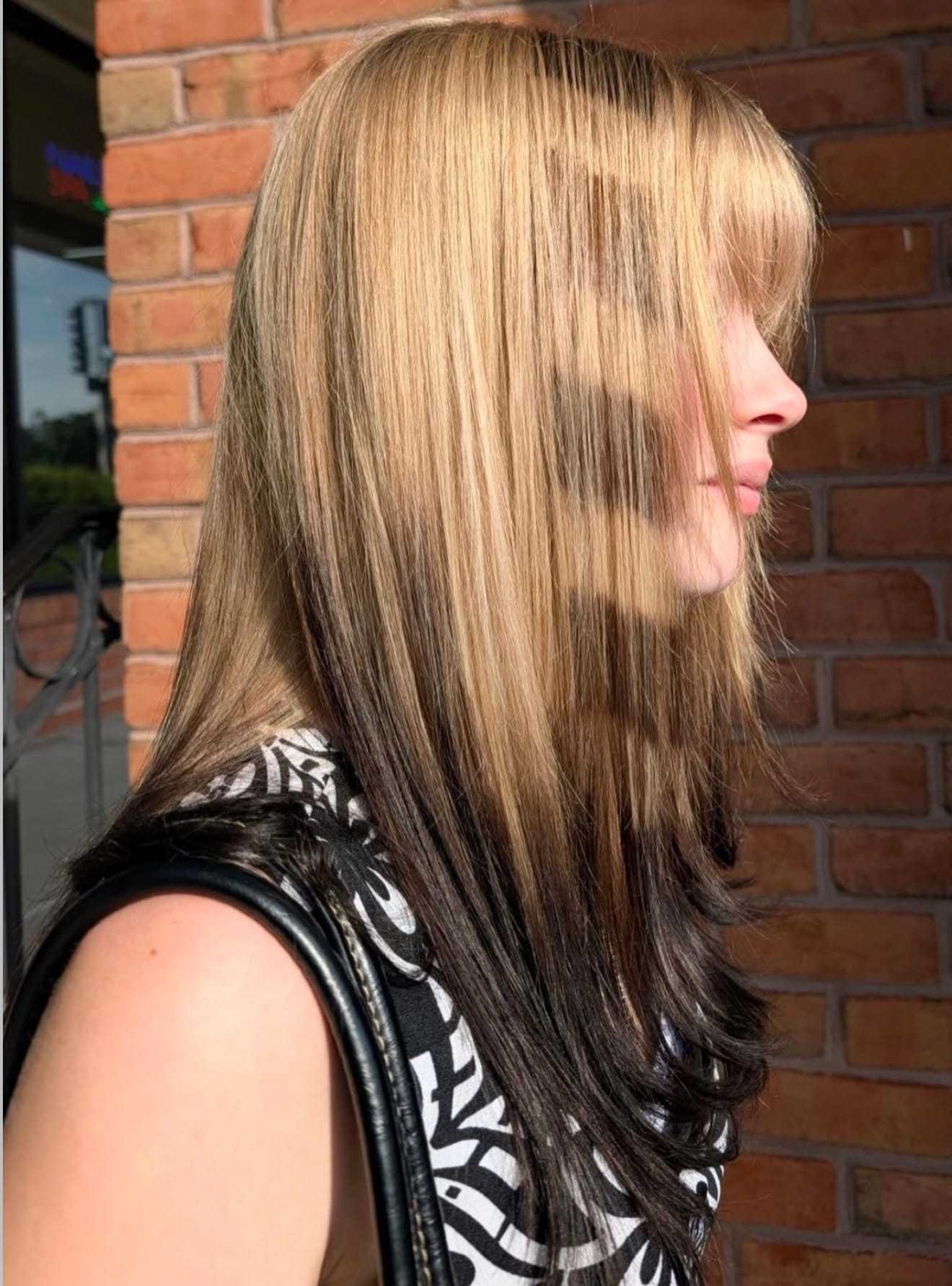 Woman with layered blonde and brown hair outside a brick building.