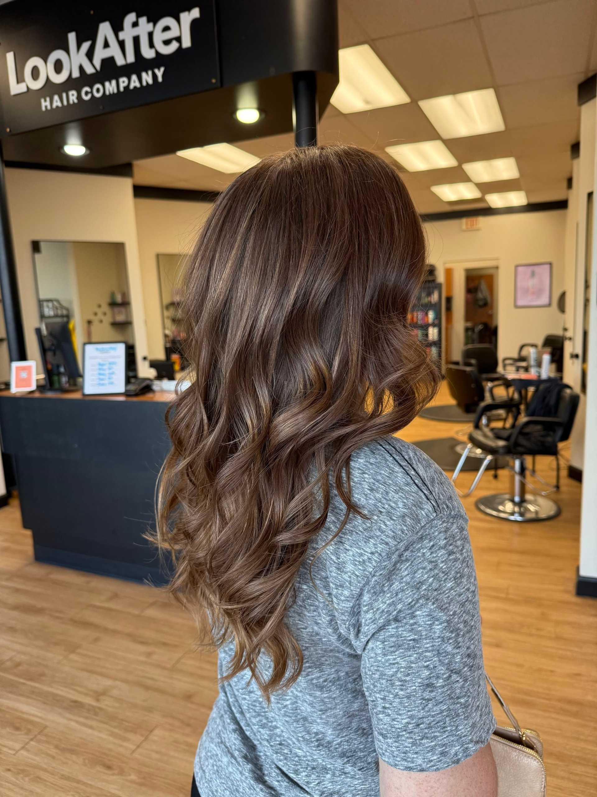 Hair salon interior with client showcasing long, wavy brown hair.