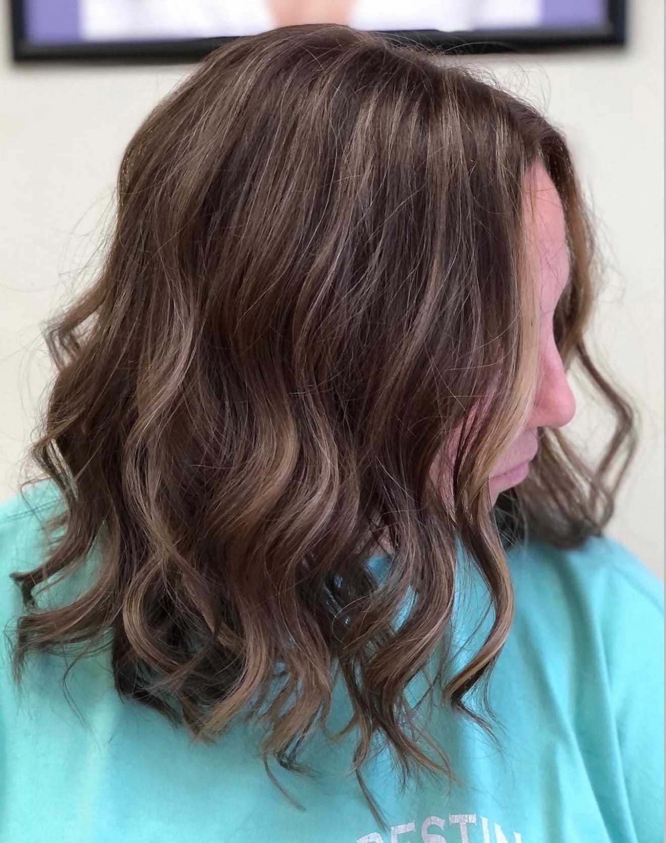 Wavy brunette hair styled in loose curls on a person wearing a turquoise shirt.