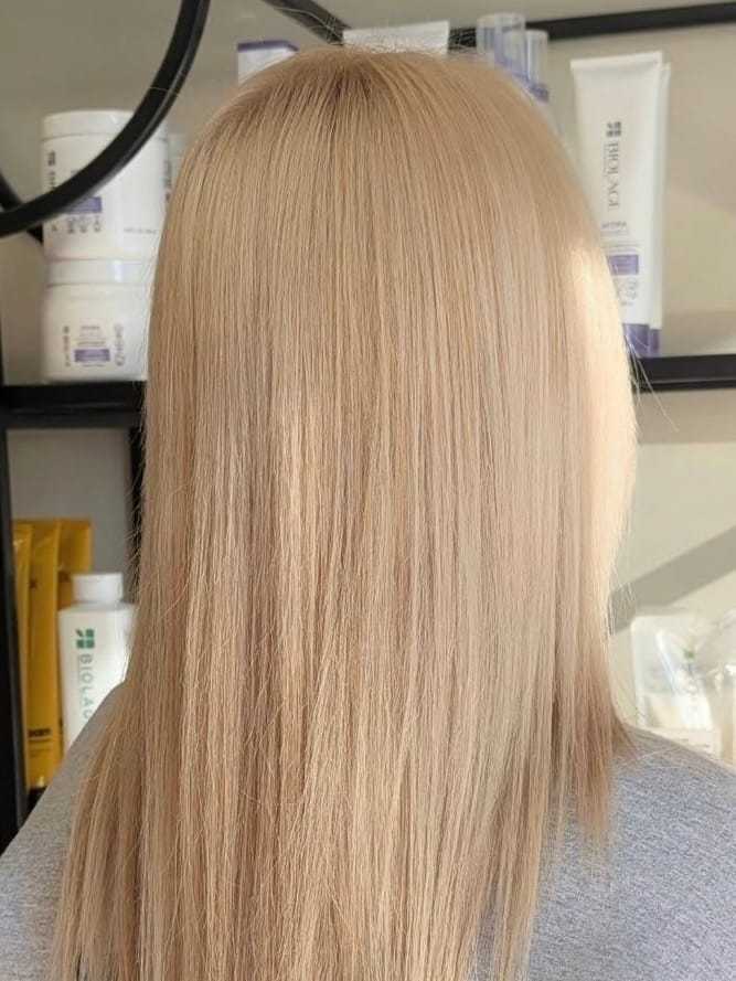 Blonde hair with smooth texture, displayed in a salon setting with product shelves in background.